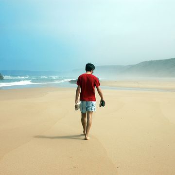 man on red shirt walking along vast and desert landscape of bordeira beach, algarve