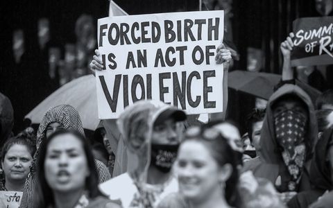 a protestor holding a sign that says forced birth is an act of violence