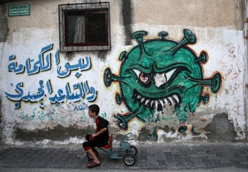 Op 29 augustus 2022 fietst een jongetje in het Palestijnse vluchtelingenkamp alShati in Gazastad langs een muurschildering van een virusdeeltje met daarbij een tekst die mensen aanspoort preventieve maatregelen te nemen tegen COVID19