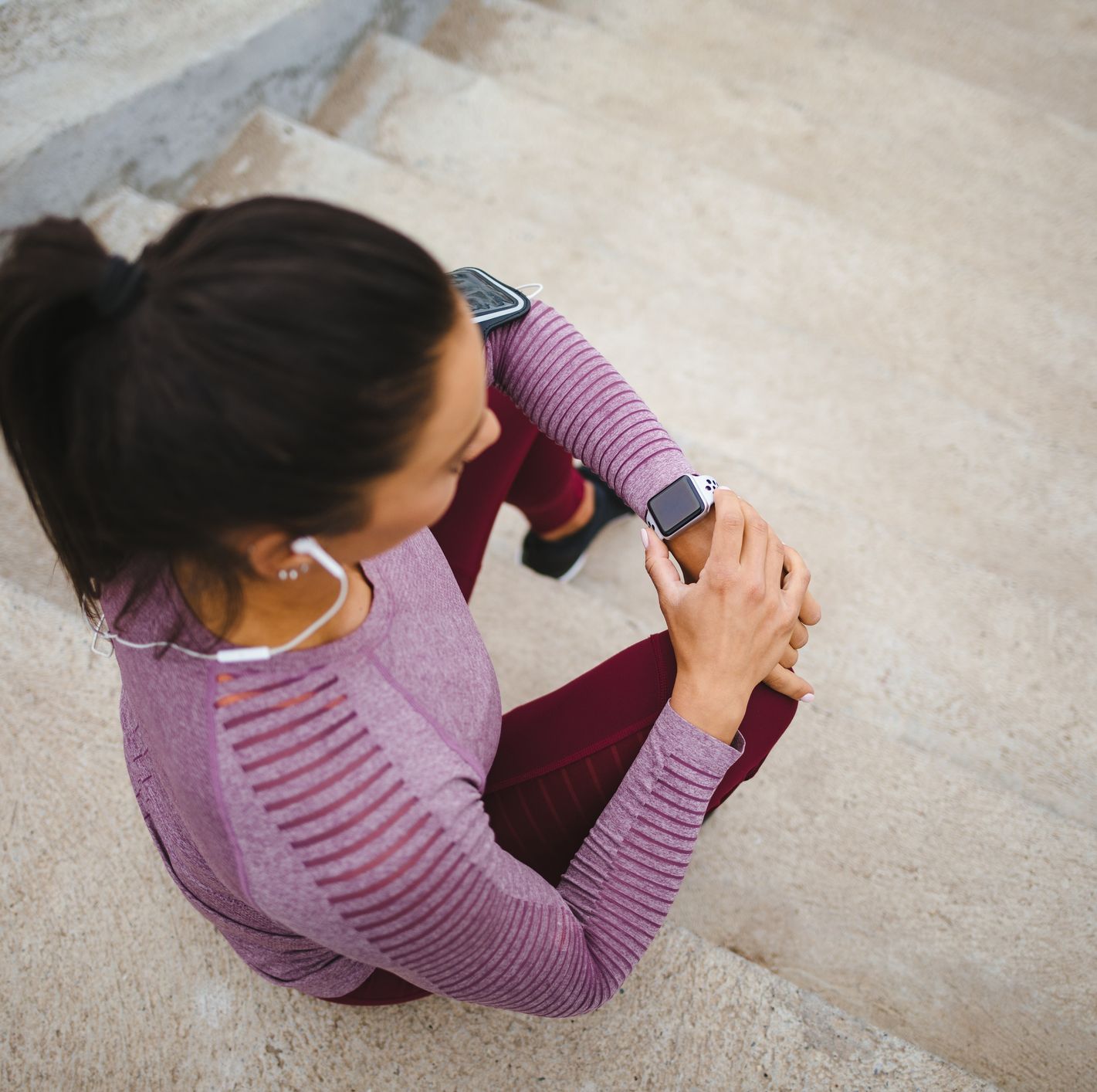 young woman sitting on the stairs and checking her running time on smart watch
