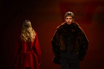 a model with short brown bangs walks towards the camera in a brown coat, while a blond model in a red coat walks in the other direction