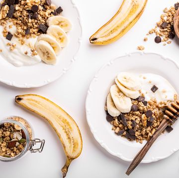 healthy breakfast with homemade granola with nuts mix, yogurt, chocolate pieces, banana and honey on white plates, top view