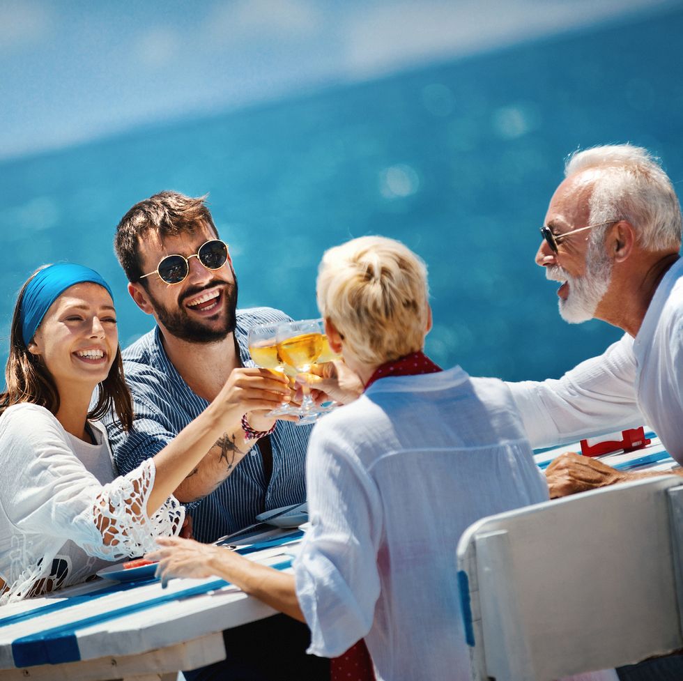 Vista lateral de cerca de una pareja de ancianos almorzando con su hijo y su prometida mientras navegan durante sus vacaciones de verano