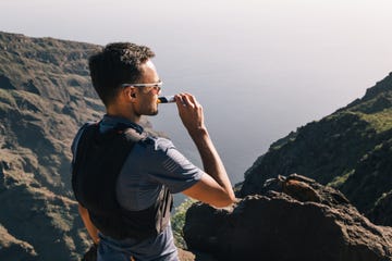 portrait of young man drinking energy sports nutrition energy gel while sitting and resting after trail running on mountain peak