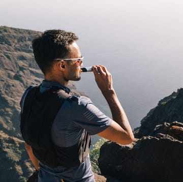 Portrait of young man drinking energy sports nutrition energy gel while sitting and resting after trail running portrait of young man drinking energy sports nutrition energy gel while sitting and resting after trail running on mountain peak