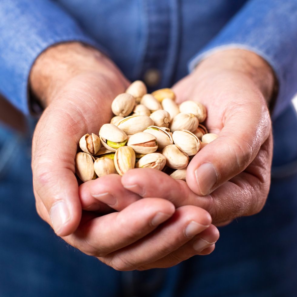 close up studio shot of mature man holding handful of pistachio nuts