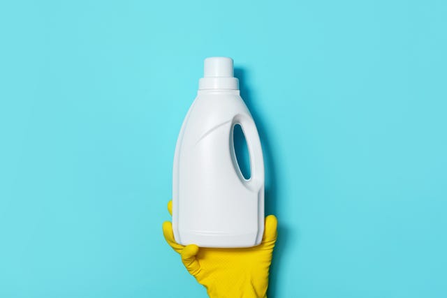 hand in glove holding white plastic bottle of cleaning product, household chemicals. copy space. cleaning service concept. household chemical cleaning products, brushes and supplies. detergent bottle.
