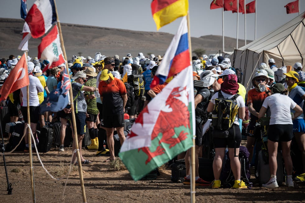 competitors arrive with their luggage to settle into the bivouac on the eve of the start of the 37th edition of the marathon des sables in the moroccan sahara desert, with different countries' flags dotted around.