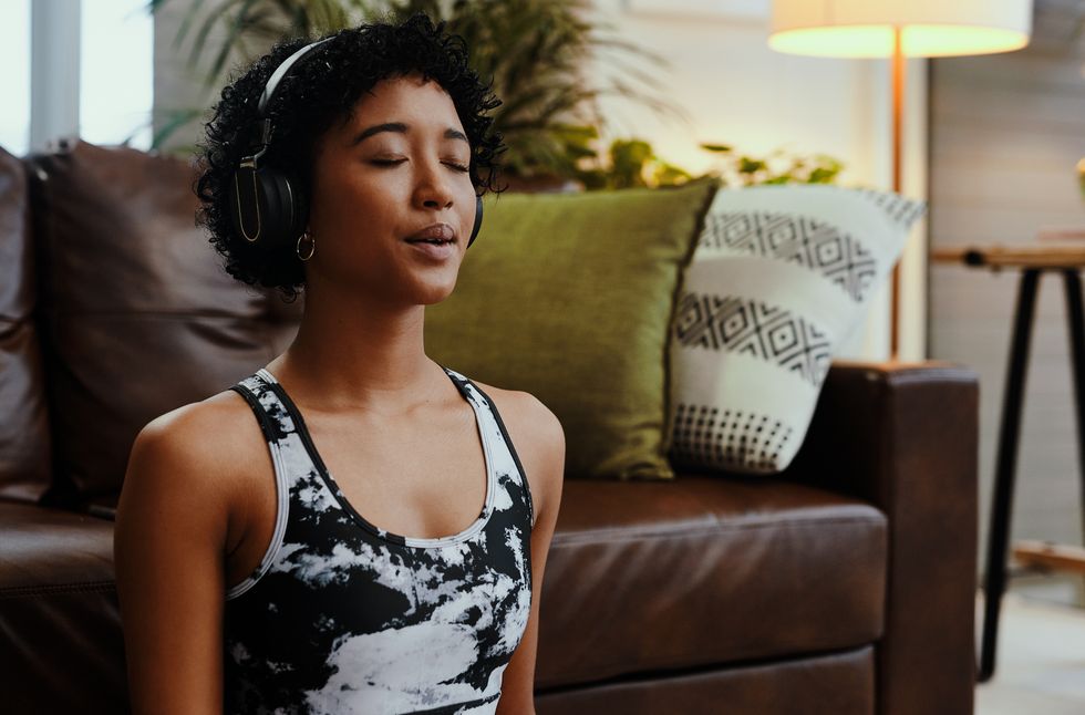 shot of a young woman listening to music while meditating at home