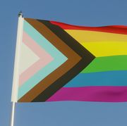 the inclusive lgbtqi pride flag with colours to include people of colour and the trans community on a flag pole in the sun