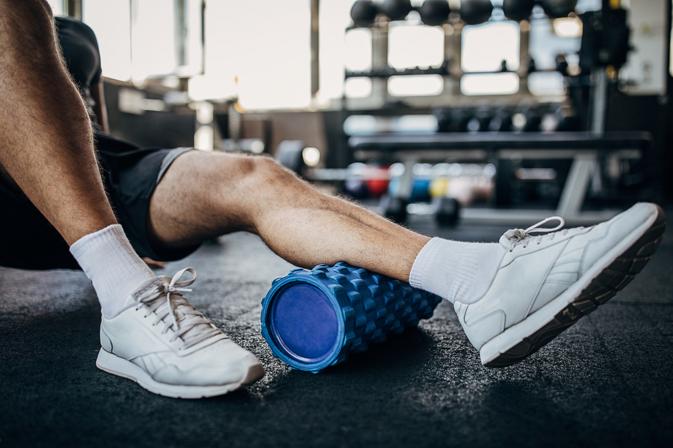 man massaging his leg muscles using a foam roller in the gym