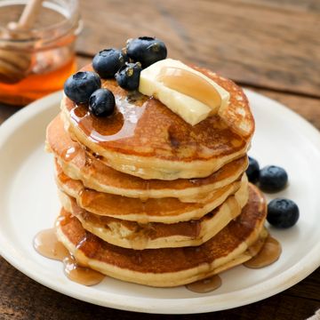 fluffy pannenkoekjes op een bord met honing, boter en blauwe bessen eroverheen
