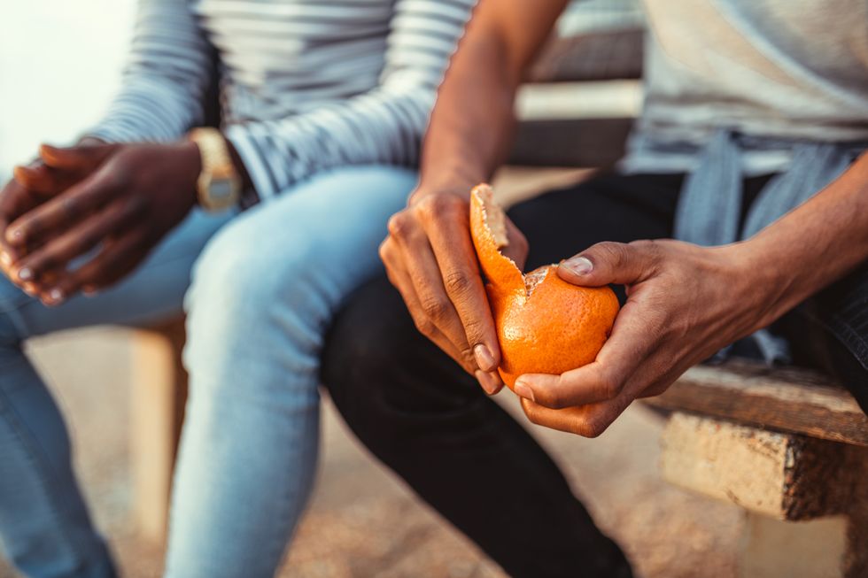 man pealing orange while sitting with a friend on the bench