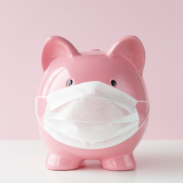 piggy bank with protective face mask on white table in front of a pink wall representing medical costs