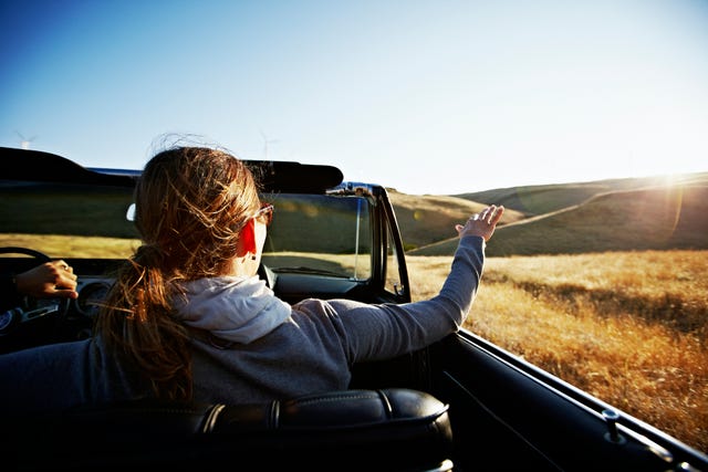 mature woman holding hand in air outside of convertible rear view