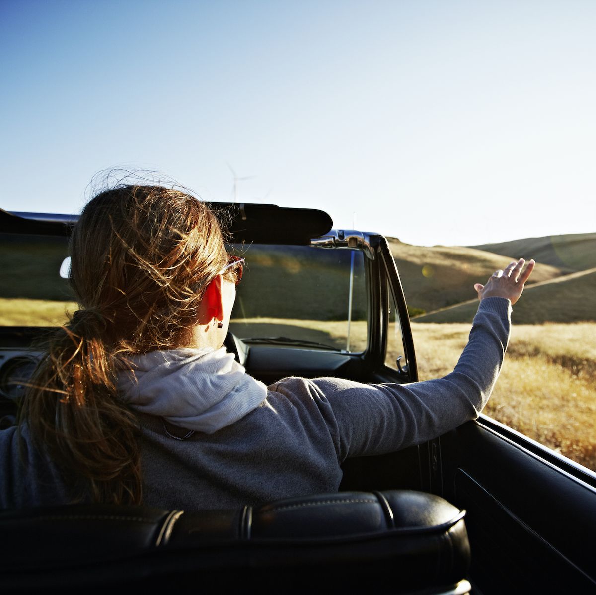 mature woman holding hand in air outside of convertible rear view