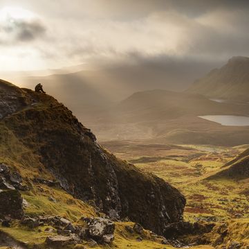 a walker sits on a viewpoint at the quiraing, a twenty four mile rock ledge on the isle of skye, scotland, uk