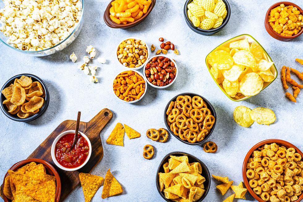 party food assortment of salty snacks in bowls shot from above on party table the composition includes potato chips, popcorn, nachos and salsa, corn bugles, pretzels, peanut, cheese sticks and others predominant colors are yellow and gray high resolution 42mp studio digital capture taken with sony a7rii and zeiss batis 40mm f20 cf lens