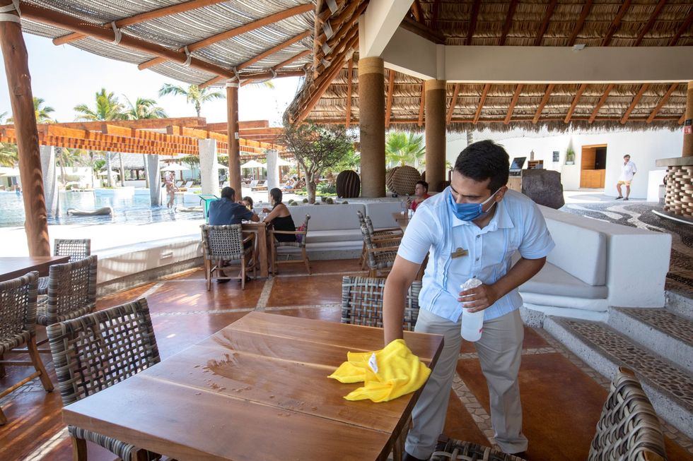 In een restaurant in La Paz Mexico ontsmet een ober een tafeltje In de toerismesector in Mexico gaan vele miljarden om maar sinds het begin van de coronaviruspandemie in maart is het aantal bezoekers aan het land ingestort