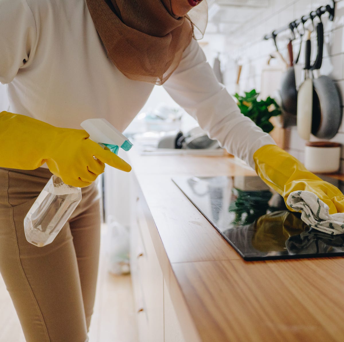 young woman cleaning up the perfect surface of black ceramic kitchen stove and counter using gloves and mop