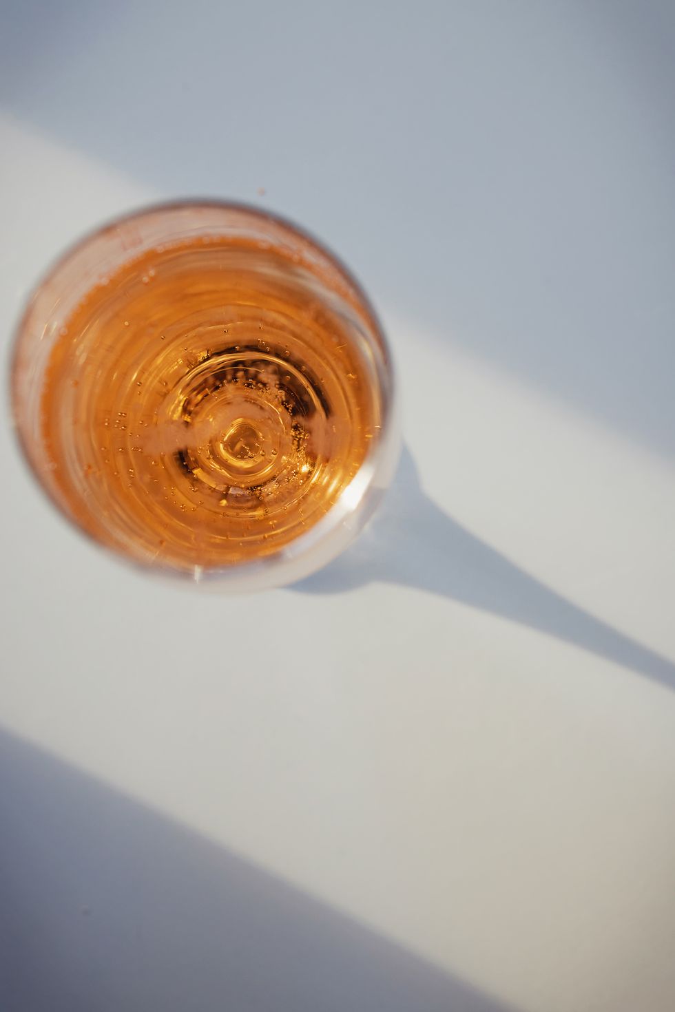 glass with rose sparkling wine on the white table with hard shadows, top view