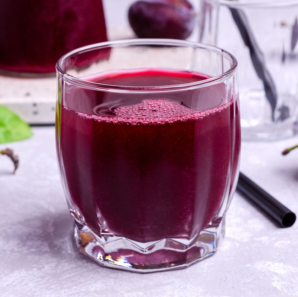 red plum juice in glass on a gray stone background with fresh fruit selective focus