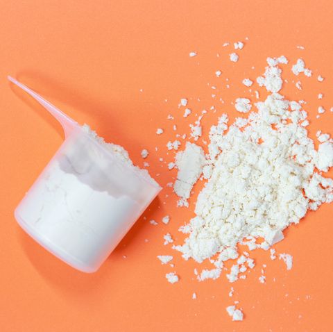 scoop with scattered protein powder, side view on a orange background