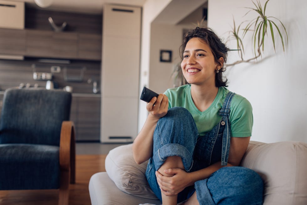 young woman sitting on the sofa, watching tv at home and enjoying