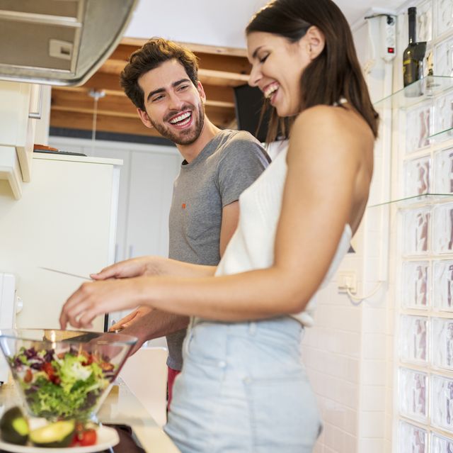 cheerful young couple preparing meal together in kitchen at home
