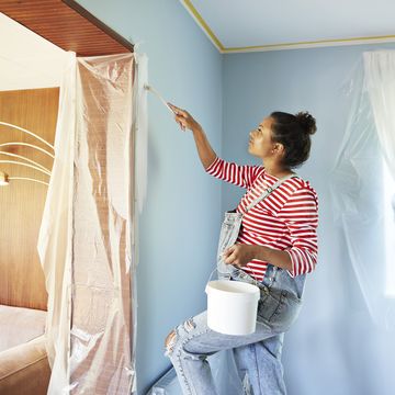 pregnant young woman holding bucket while applying paint on wall at home