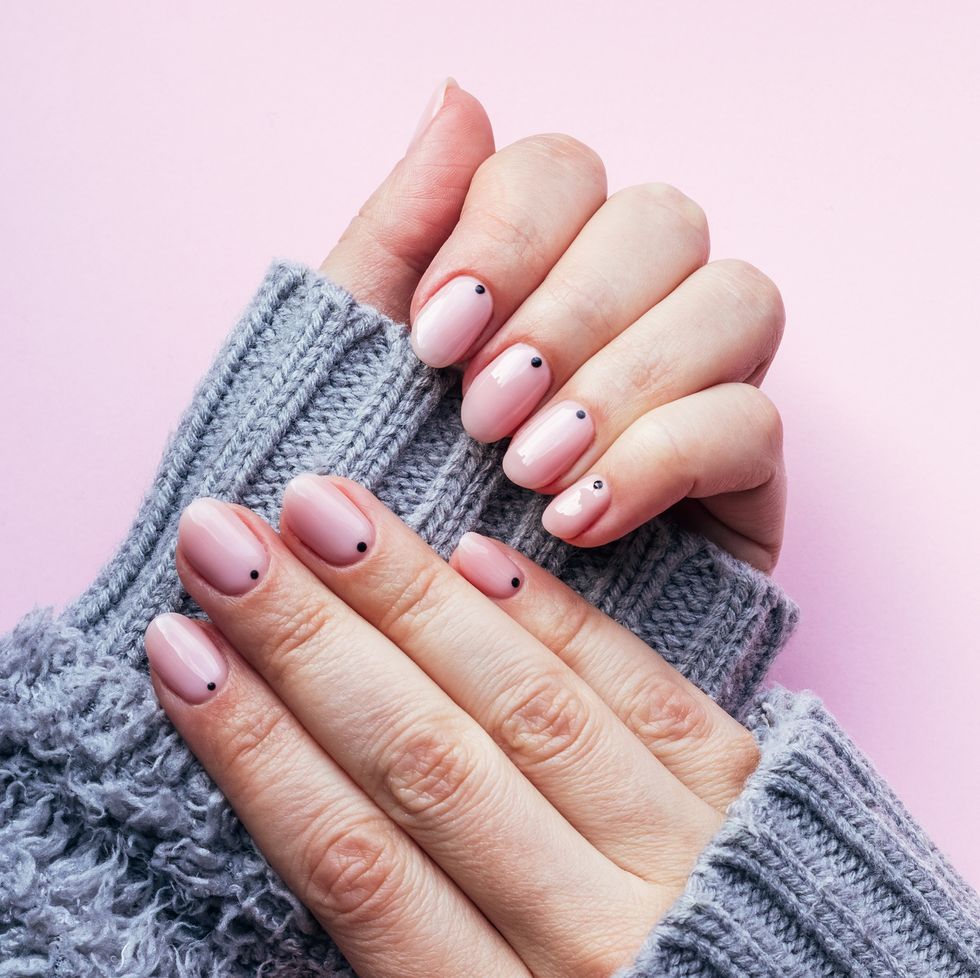 female hands in a gray fluffy knitted sweater with trendy beautiful manicure pink nude nails with black small dots on a pink background with copy space