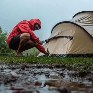man camping fixing tent on rainy day