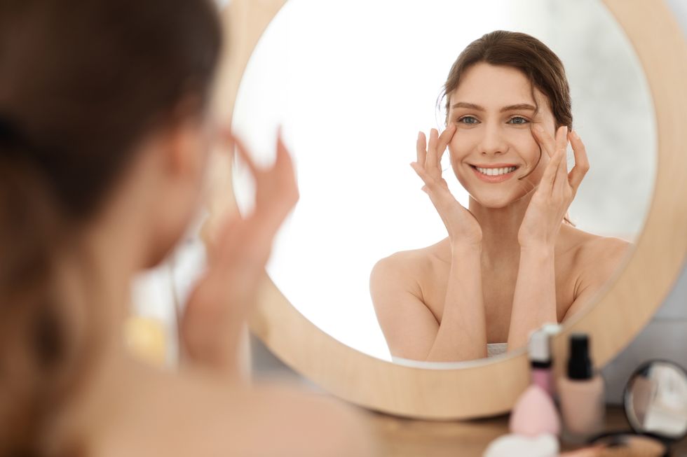 eye care routine young woman massaging eye zone, looking at mirror, home interior