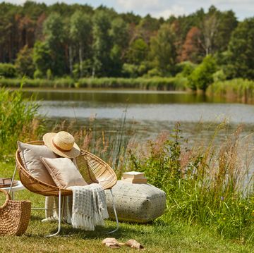 stylish composition of outdoor garden on the lake with design rattan armchair and elegant accessories summer chillout mood