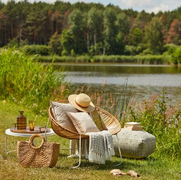 stylish composition of outdoor garden on the lake with design rattan armchair and elegant accessories summer chillout mood