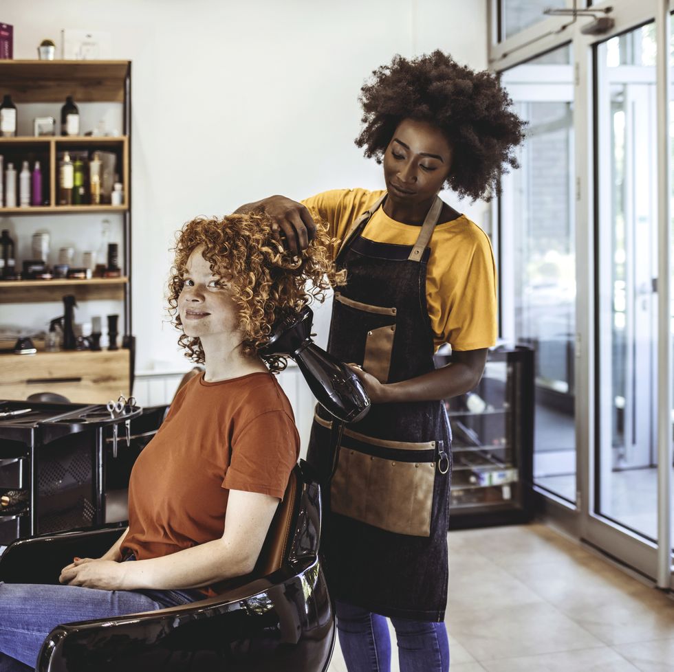 african hairdresser drying womans hair with hair dryer in beauty salon