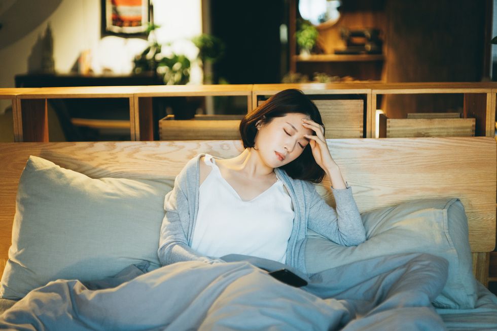young asian woman feeling sick and suffering from a headache, lying on the bed and taking a rest at home