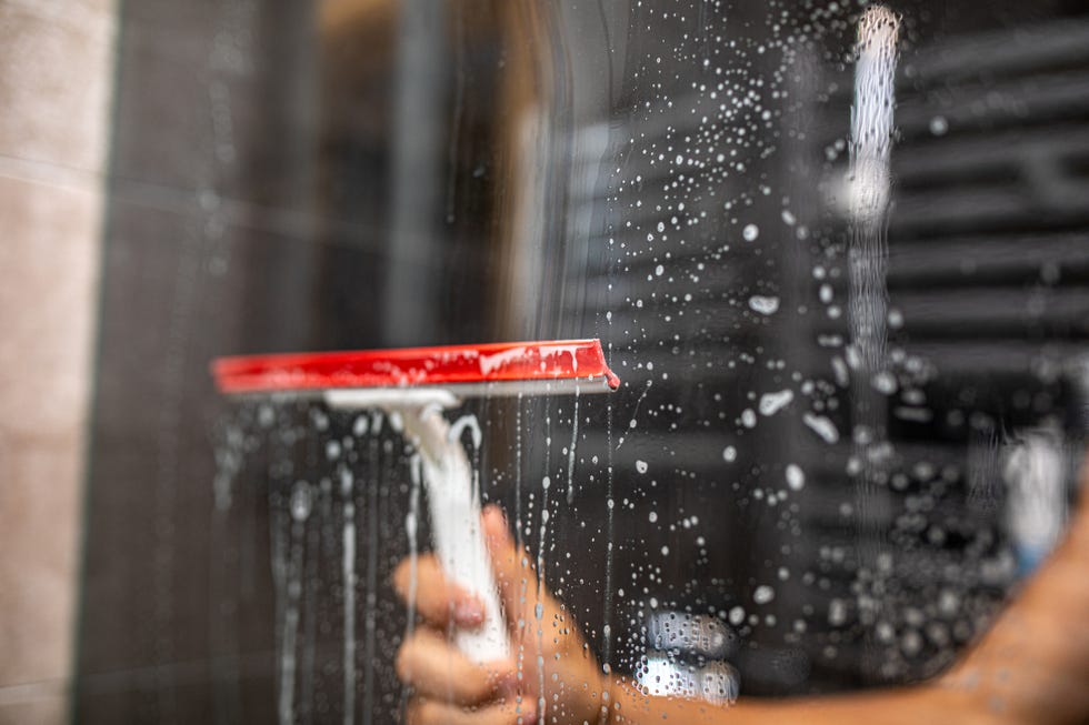 male hand cleaning glass window pane in bathroom with shower squeegee