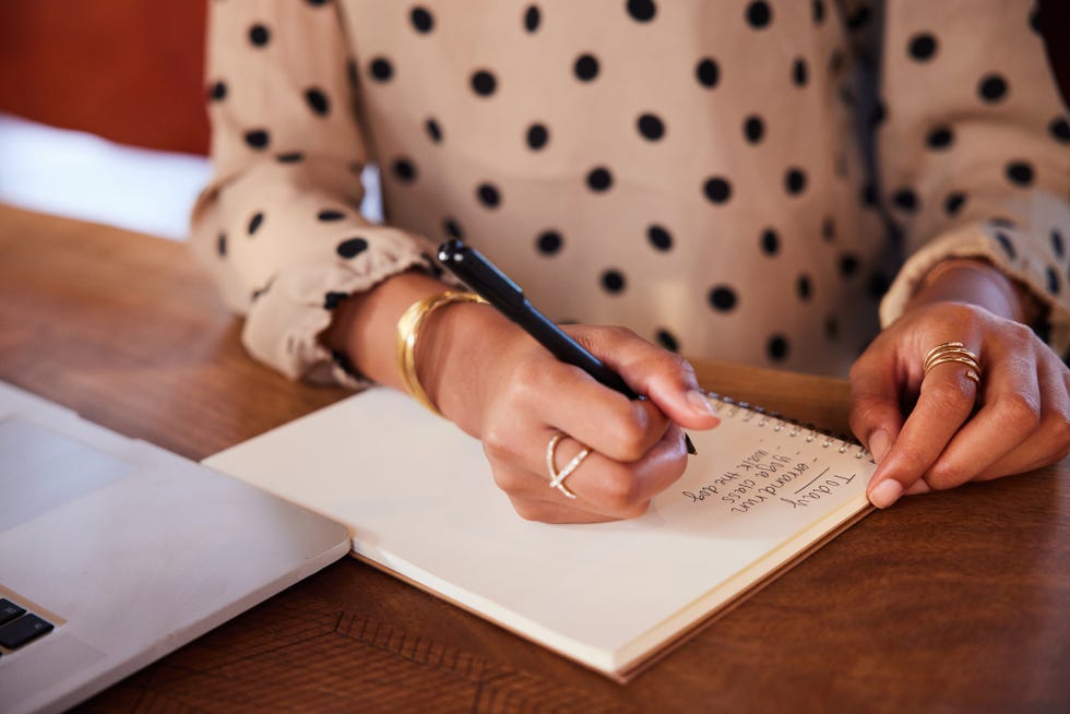 close up of an african american businesswoman writing on a notepad and working on a laptop at a table in a cafe