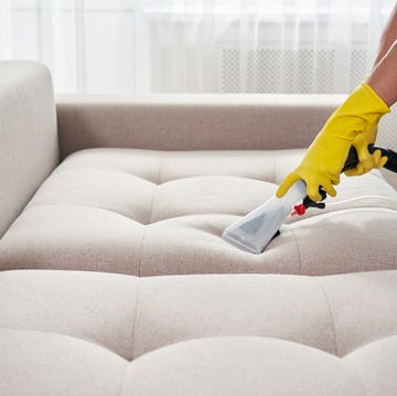 Close-up of housekeeper holding modern washing vacuum cleaner and cleaning dirty sofa with professionally detergent. Professional springclean at home concept dry cleaning worker removing dirt from sofa indoors