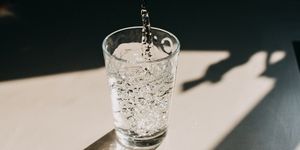 water being poured in a glass of water that cast a beautiful shadow on a white kitchen countertop copy space