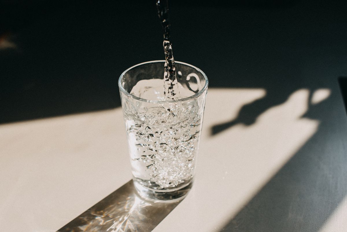 water being poured in a glass of water that cast a beautiful shadow on a white kitchen countertop copy space