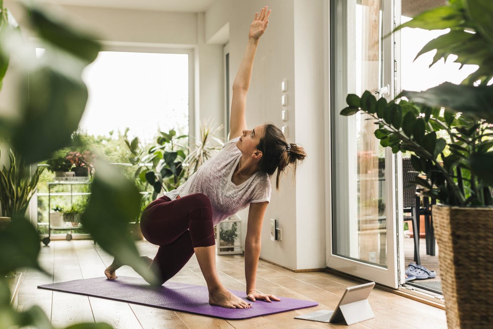 young woman with digital tablet exercising on mat at home