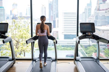 rear view of fitness woman running on treadmill during a cardio session against city view in a health club