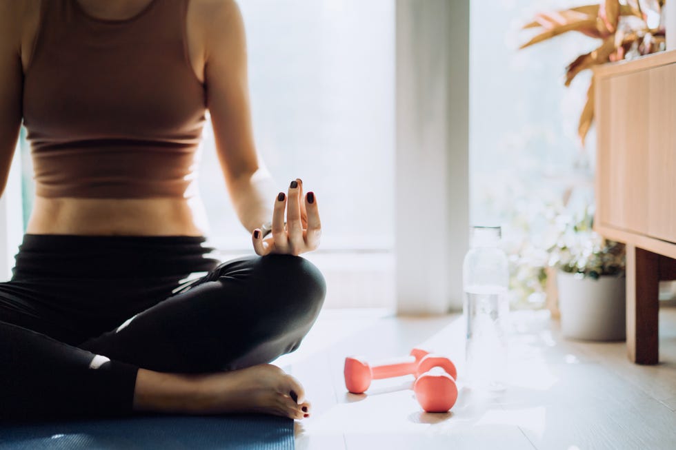 cropped shot of young asian woman sitting on the exercise mat, meditating in the lotus pose during a yoga session at home in the fresh bright morning fitness, wellness and home work out concept