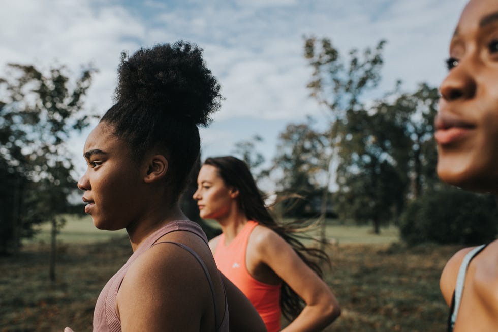 strong, fit woman joggers, running through a sunny park at sunrise. they look determined as they put in the effort. their hair blows behind them as they look in front of them. space for copy.