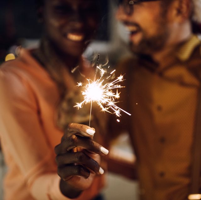 close up of couple celebrating new year and having fun with sparklers while drinking champagne at home