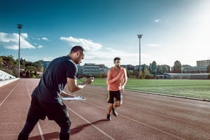 runner and coach doing sports training on track and field the coach is measuring results with a stopwatch