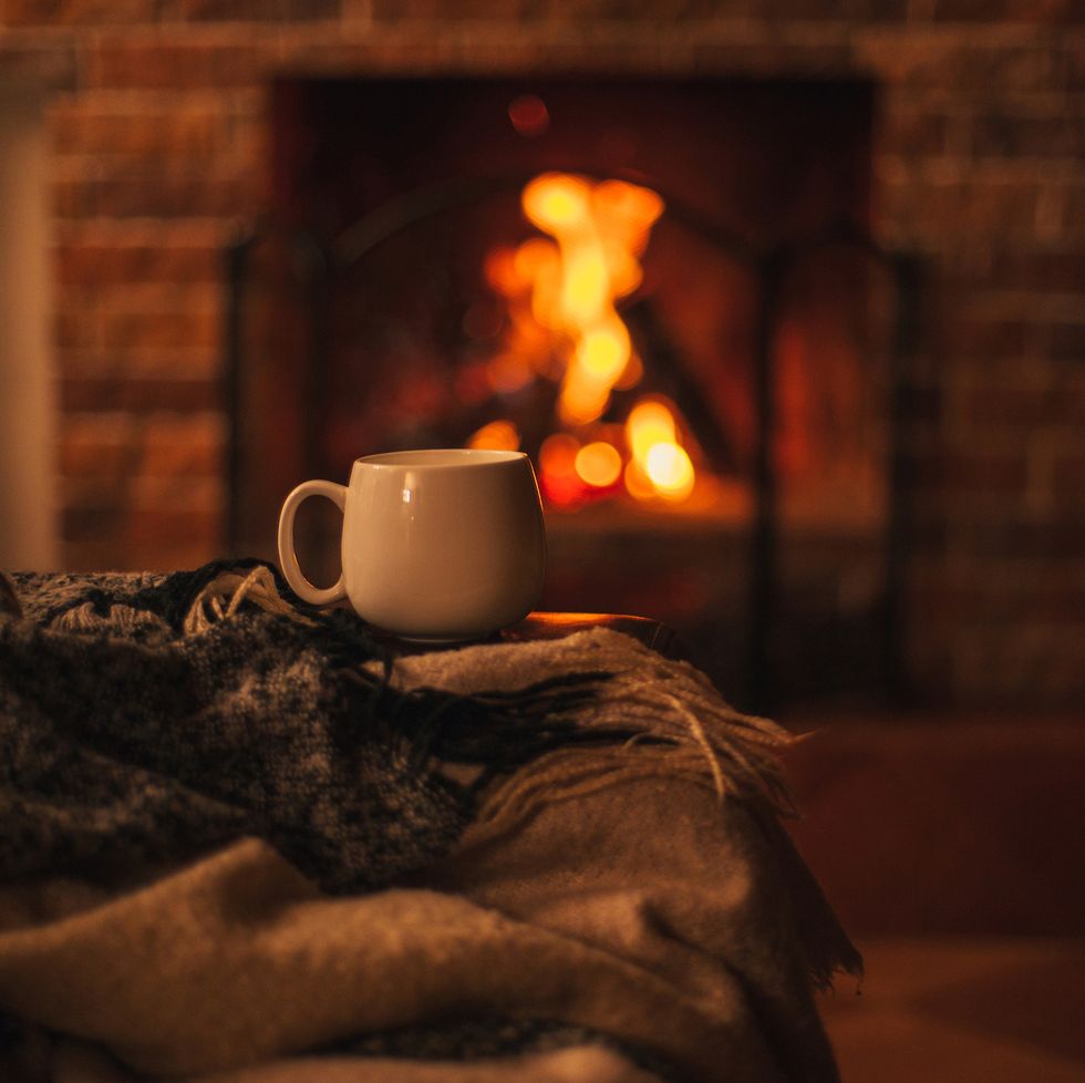 mug with hot tea standing on a chair with woolen blanket in a cozy living room with fireplace cozy winter day