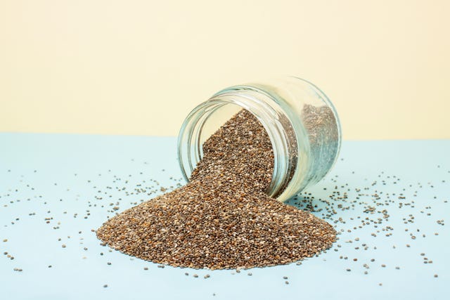 chia seeds spilling out of a glass jar on a blue yellow background healthy food concept, superfood, dietary supplements